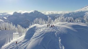 Skiers stand and celebrate atop the snowy mountains as Redal's drone soars overhead. Photo courtesy: Screenshot from Above Bellingham.