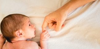 Newborn baby securely grasping his mother's hands, close-up fingers.
