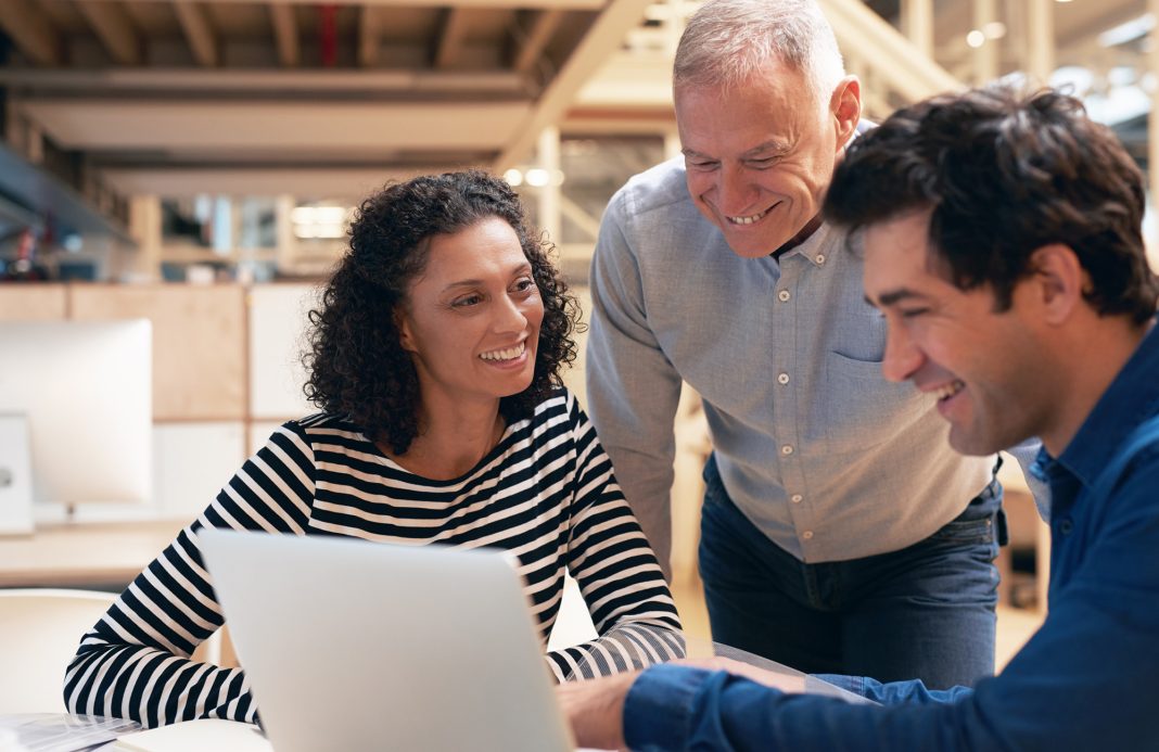 Smiling coworkers talking together over a laptop in an office