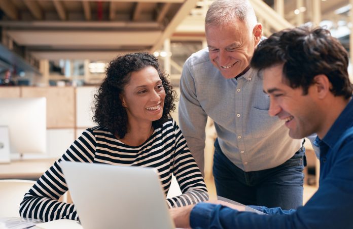 Smiling coworkers talking together over a laptop in an office