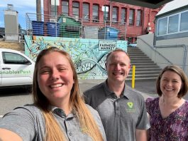 Marranda, Alex and Juliana pose for a selfie in front of a Venables truck and wall art with a blue design and the words Bellingham Farmers Market on it