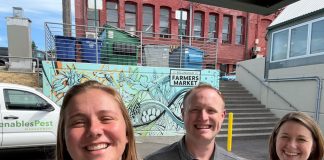 Marranda, Alex and Juliana pose for a selfie in front of a Venables truck and wall art with a blue design and the words Bellingham Farmers Market on it