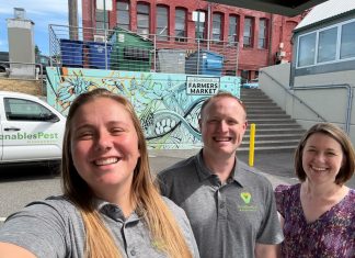 Marranda, Alex and Juliana pose for a selfie in front of a Venables truck and wall art with a blue design and the words Bellingham Farmers Market on it